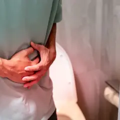 Osoba trzyma się za brzuch, odczuwając ból przy oddawaniu moczu. W tle widoczna jest toaleta.